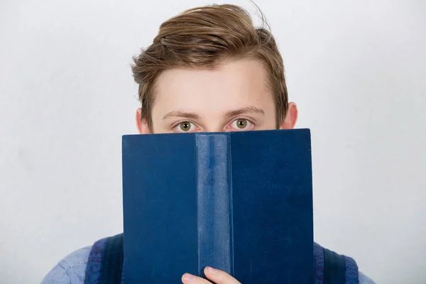 Gestresste Studentin bedeckt das halbe Gesicht mit einem aufgerissenen blauen Buch. dif — Stockfoto