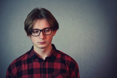 Sad and disappointed teenage boy, wearing red shirt and glasses,