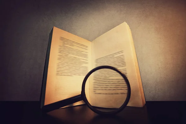 Close-up de um livro aberto sobre a mesa e uma lupa — Fotografia de Stock