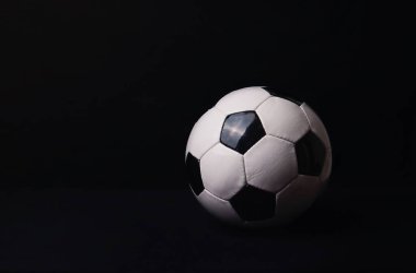 Reklam ve reklam için fotokopi alanı olan siyah bir arka planda izole edilmiş klasik futbol topu. Gerçek fotoğraf, siyah duvarın üzerinde geleneksel futbol topu sembolü..