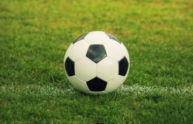 Klasik futbol topu, tipik siyah-beyaz altıgen desenli, stadyum sahasına yerleştirilmiş. Geleneksel futbol topu yeşil çimenlik alanda.