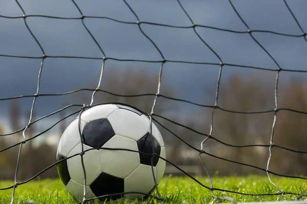 Close up of a soccer ball behind the gates net, goal scoring concept. Outdoors football match, practicing spring sports. Healthy activity and games, green turf background.
