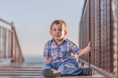 Köprüde havuzun üzerinde günbatımında oturan çocuk