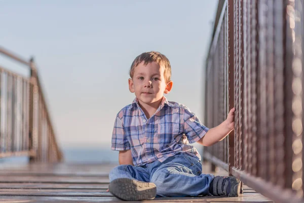 Köprüde havuzun üzerinde günbatımında oturan çocuk