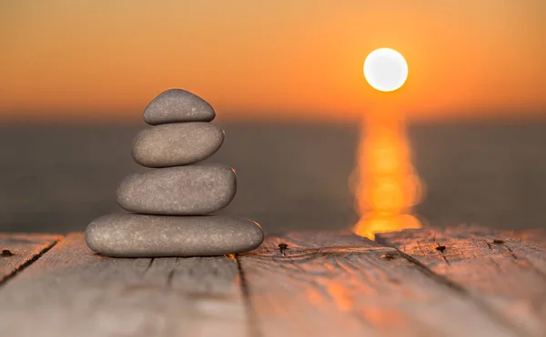 Gestapelte Kieselsteine auf einer Holzoberfläche und untergehende Sonne — Stockfoto