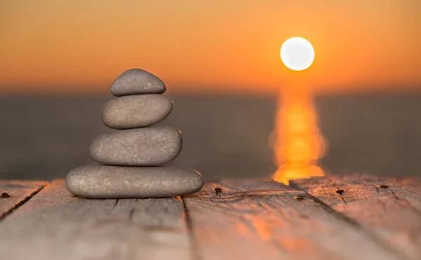 Guijarros apilados sobre una superficie de madera y sol poniente — Foto de Stock