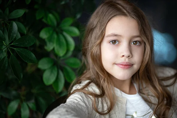 Beautiful white girl looks at us and smiles on a background of green leaves — Stock Photo, Image