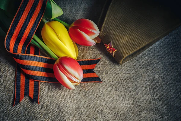 Военная шапочка с орденом Великой Отечественной войны и цветы тюльпанов, перевязанные Георгиевской лентой — стоковое фото