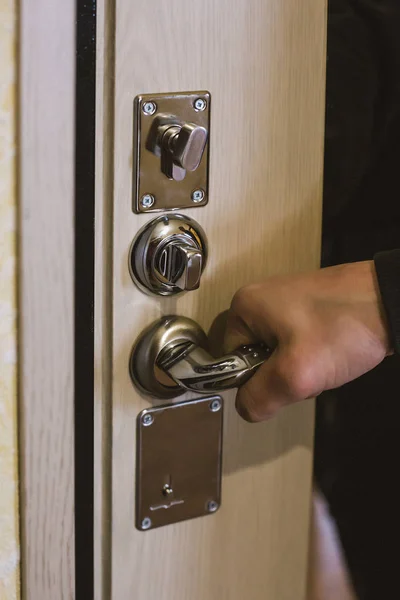 Mano masculina abriendo una puerta interior de madera clara con una vista de cerca de su mano en el mango de metal por encima de una cerradura circular y cerradura, espacio de copia por debajo — Foto de Stock