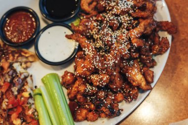 dilimlenmiş tavuk göğsü kotletpane ve derin kızarmış tavuk parçaları, susam, krem ve domates sosu serpilir, teriyaki sosu, kereviz kök bir plaka üzerinde sebzeli pizza dilimleri.