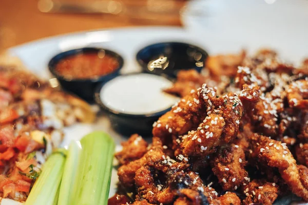 dilimlenmiş tavuk göğsü kotletpane ve derin kızarmış tavuk parçaları, susam, krem ve domates sosu serpilir, teriyaki sosu, kereviz kök bir plaka üzerinde sebzeli pizza dilimleri.