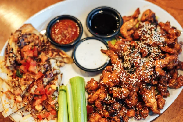 dilimlenmiş tavuk göğsü kotletpane ve derin kızarmış tavuk parçaları, susam, krem ve domates sosu serpilir, teriyaki sosu, kereviz kök bir plaka üzerinde sebzeli pizza dilimleri.