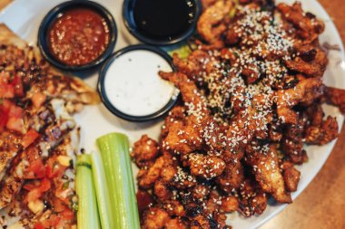 dilimlenmiş tavuk göğsü kotletpane ve derin kızarmış tavuk parçaları, susam, krem ve domates sosu serpilir, teriyaki sosu, kereviz kök bir plaka üzerinde sebzeli pizza dilimleri.