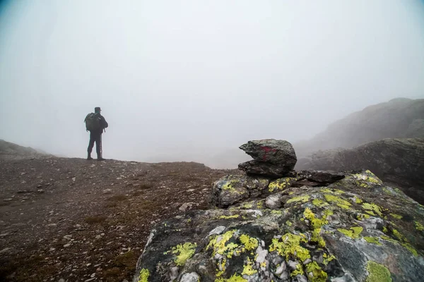 People in fog on mountain. Hiker climbed on peak of rock above foggy valley. In the foreground a signpost like a pyramid from stones