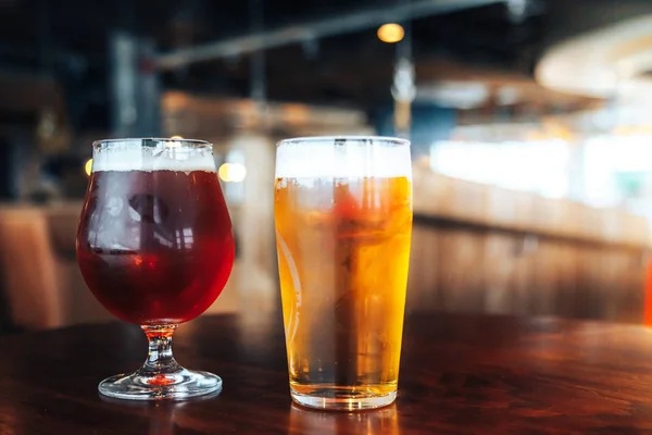 Dos vasos de cerveza clara y oscura sobre una mesa de madera en un café o — Foto de Stock