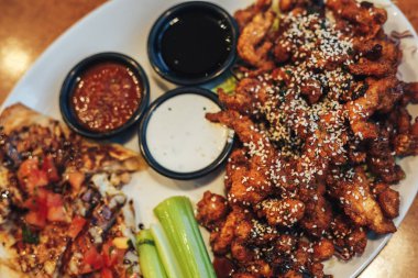 dilimlenmiş tavuk göğsü kotletpane ve derin kızarmış tavuk parçaları, susam, krem ve domates sosu serpilir, teriyaki sosu, kereviz kök bir plaka üzerinde sebzeli pizza dilimleri.