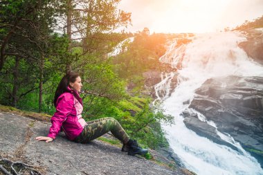 Taş üzerine oturan bir genç uzun yürüyüşe çıkan kimse kız ve şelaleler Norveç vadisinde bir şelale hayran