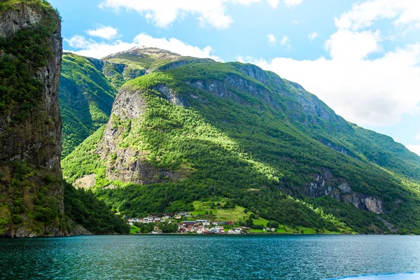 Pequeño pueblo con un hermoso telón de fondo en Flam Fjords, Noruega. Montañas y fiordo en Noruega. Nubes y cielo azul. Hermosas vistas impresionantes de las montañas, el agua, el cielo, las nubes y el sol. Naturaleza noruega . — Foto de Stock