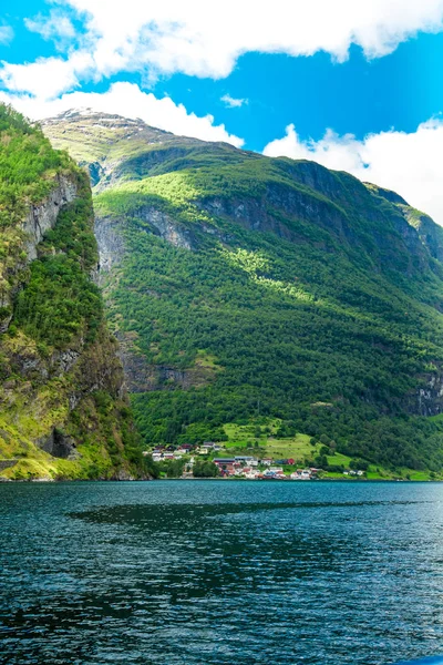 Pequeño pueblo con un hermoso telón de fondo en Flam Fjords, Noruega. Montañas y fiordo en Noruega. Nubes y cielo azul. Hermosas vistas impresionantes de las montañas, el agua, el cielo, las nubes y el sol. Naturaleza noruega . — Foto de Stock
