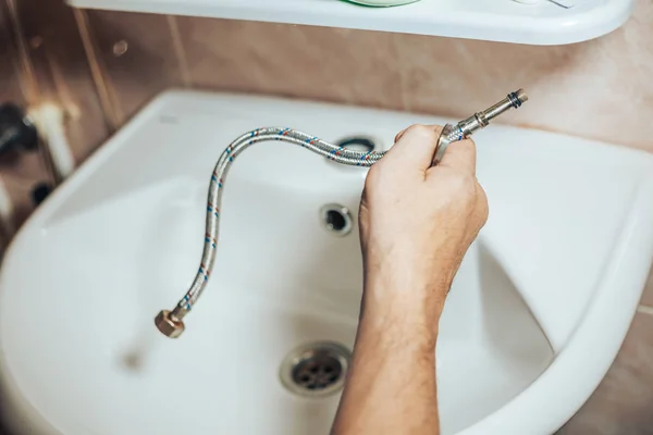 Servicios de hombre y reparaciones fugas grifo viejo en el grifo en el baño. Hombre sosteniendo una manguera para grifo — Foto de Stock