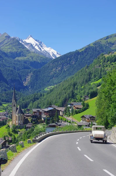 Old retro car driving in the Austria Alps. Heiligenblut church a — Stock Photo, Image