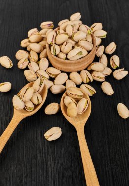 Siyah ahşap arka planda bir kasede fıstıklar.                                  