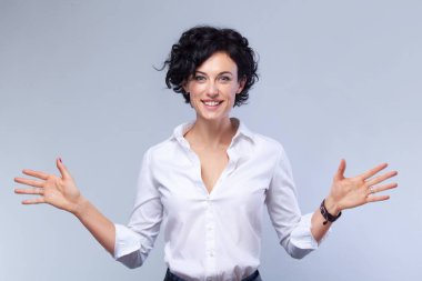 Mutlu genç esmer gri arka plan kopya alanı arıyor Kollarını açarak kamera ile işkadını kıvırcık saç