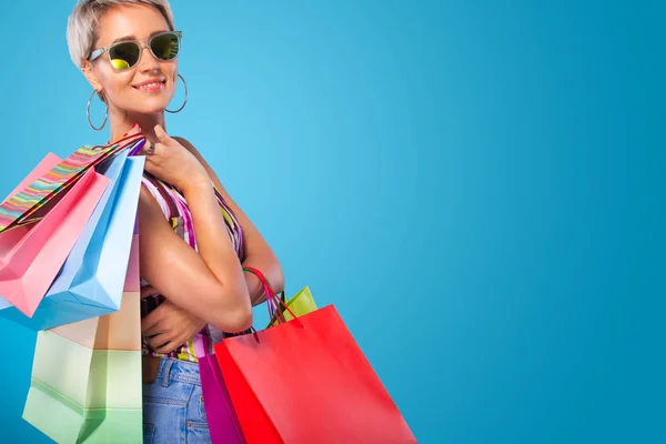 Shopping kvinna som håller färgen väskor isolerad på blå bakgrund i svart fredag semester. Sommar försäljning koncept. — Stockfoto