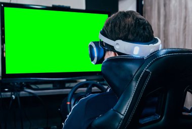 Genç adam sanal gerçeklik gözlükleriyle simülatör koltuğu ve direksiyonda oyun oynuyor. Krom anahtar yeşil ekran