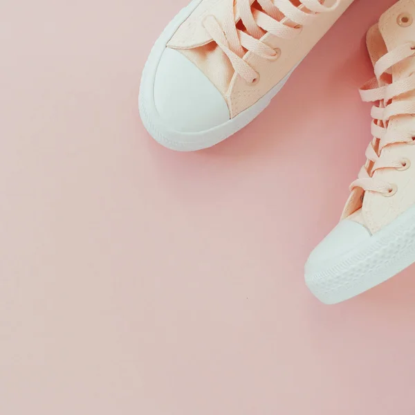 Flat lay of female sneakers on a pale pink pastel background. Place for your design, text, etc.