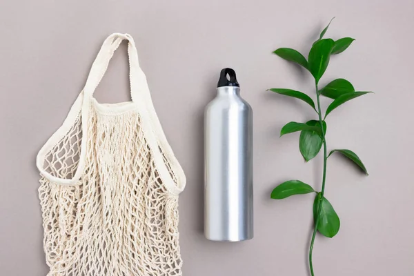 Layout of reusable shopping bag with green ruscus branch and metal bottle. Plastic free concept.