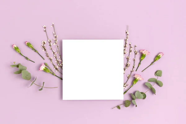 Frame made of eucalyptus and flowers on a purple pastel background. Paper card mockup. Holiday concept.