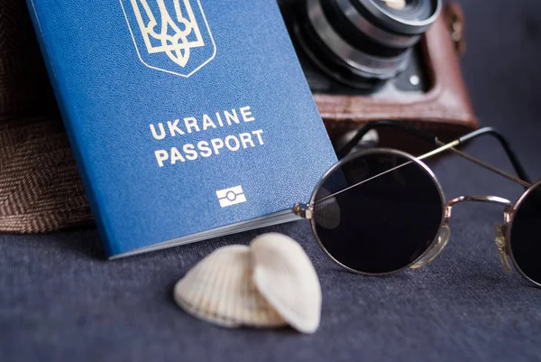 Ukraiński paszport na szarym tle. Okulary przeciwsłoneczne, kapelusz. Vintage aparatu na tle. Wiza UE bezpłatny dostęp. Płytkiej głębi ostrości, ostrość na ukraiński logo na paszport. — Zdjęcie stockowe
