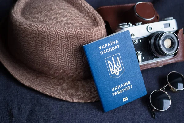 Pasaporte de viaje ucraniano sobre fondo gris. gafas de sol, sombrero. cámara vintage en el fondo. Acceso sin visado a la UE. Profundidad superficial del campo, enfoque en el logotipo ucraniano en el pasaporte . —  Fotos de Stock