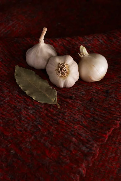 Garlic, bay leaf, black pepper on a red textile. Food background. Garlics. sliced garlic, garlic clove, garlic bulb.