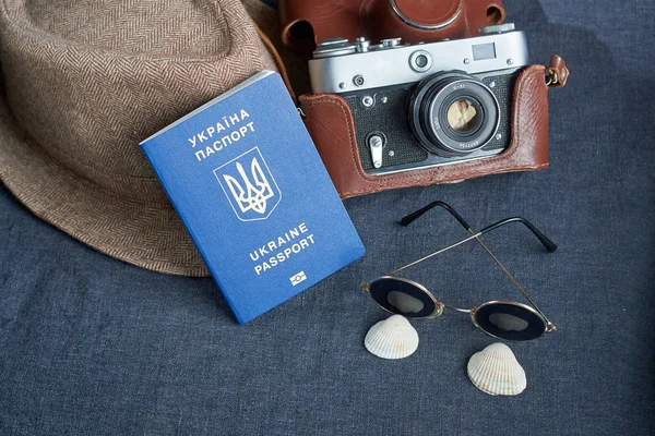 Paspor perjalanan Ukraina dengan latar belakang abu-abu. Kacamata hitam, topi. kamera vintage di latar belakang. Visa Uni Eropa akses bebas. Bidang yang dalam, fokus pada logo Ukraina pada paspor . — Stok Foto