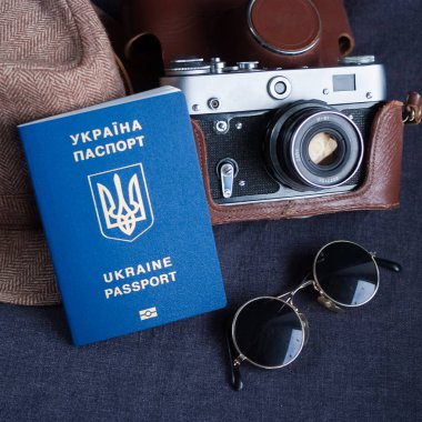 Ukrainian travel passport on gray background. sunglasses, hat. vintage camera on the background. EU visa free access. Shallow depth of field, focus on the Ukrainian logo on the passport. clipart