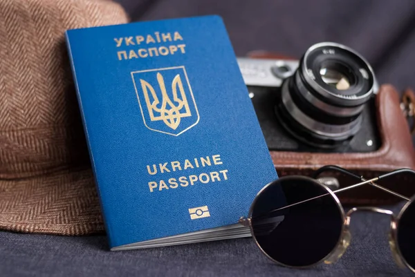 Ukraiński paszport na szarym tle. Okulary przeciwsłoneczne, kapelusz. Vintage aparatu na tle. Wiza UE bezpłatny dostęp. Płytkiej głębi ostrości, ostrość na ukraiński logo na paszport. — Zdjęcie stockowe