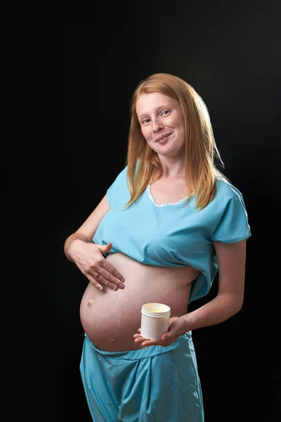 Glad gravid kvinna med magkräm. Förebyggande av bristningar. Graviditet och hudvård. mage gravid kvinna och leende från fuktgivande kräm för bristningar — Stockfoto