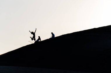 İnsanlar kum tepeleri üzerinde atlama