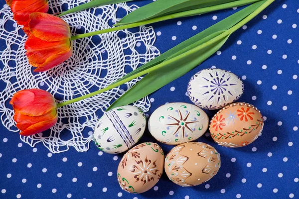 Ovos de Páscoa coloridos com tulipas na toalha de mesa azul . — Fotografia de Stock
