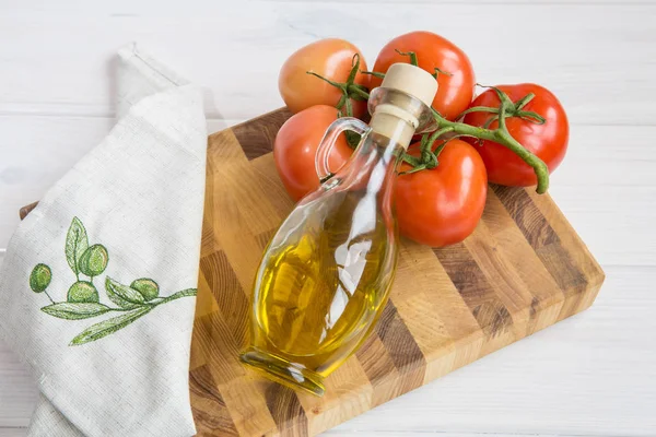 Aceite de oliva y una rama de tomates sobre un fondo de madera de color blanco — Foto de Stock