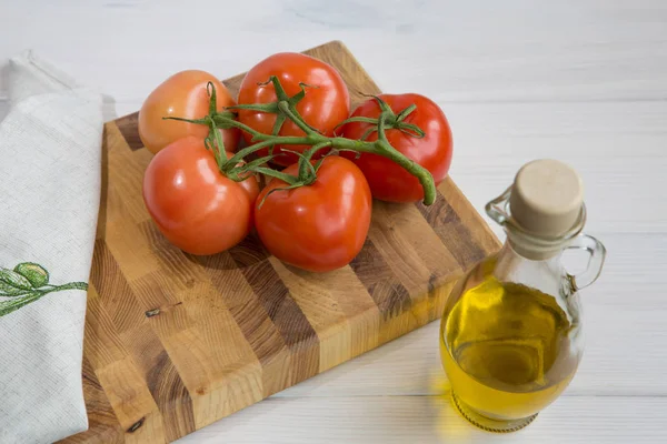 Aceite de oliva y una rama de tomates sobre un fondo de madera de color blanco — Foto de Stock