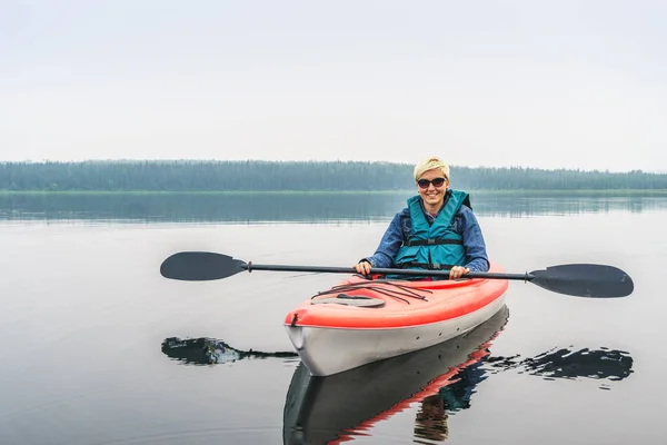在太阳镜享受红皮划艇从湖中的女人 — 图库照片