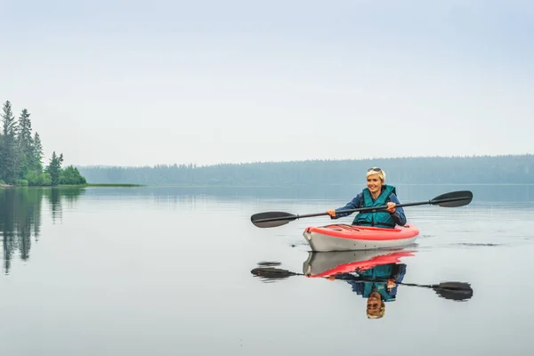 Frau paddelt glücklich aus rotem Kajak auf ruhigem See — Stockfoto