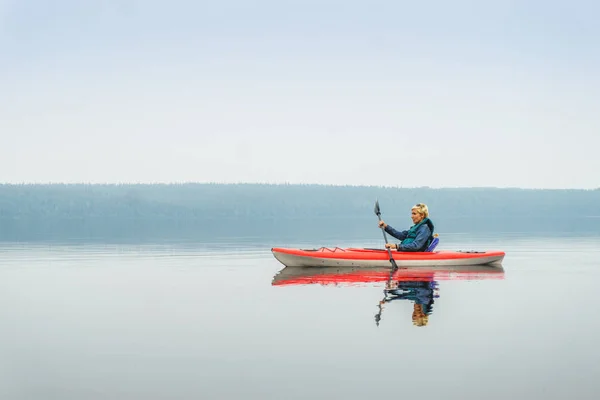 Mulher feliz para remar de caiaque vermelho no lago calmo — Fotografia de Stock