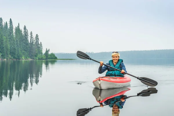 Mulher feliz para remar de caiaque vermelho no lago calmo — Fotografia de Stock