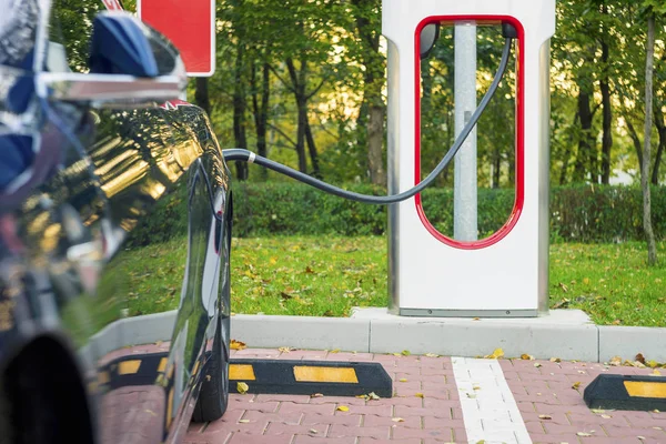 Moderne elektrische auto die zijn aangesloten op het laadstation op een parkeerplaats — Stockfoto