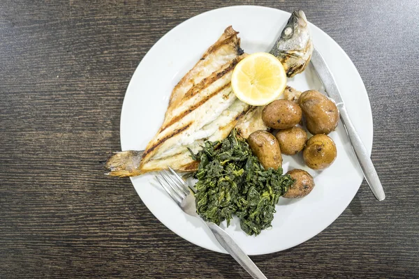 Branzino alla brace servito con limone, patate al forno e spinaci — Foto Stock