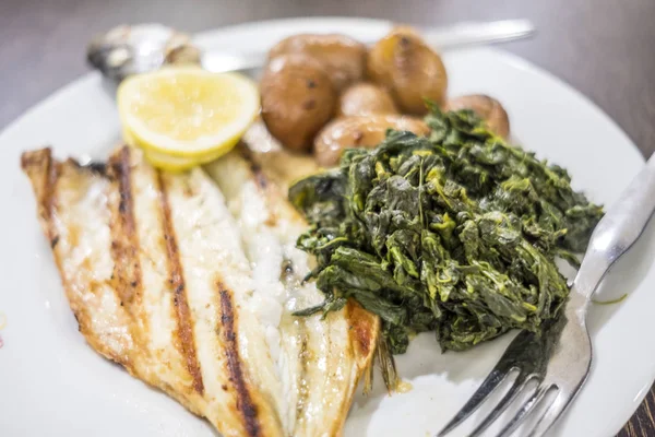 Branzino alla brace servito con limone, patate al forno e spinaci — Foto Stock